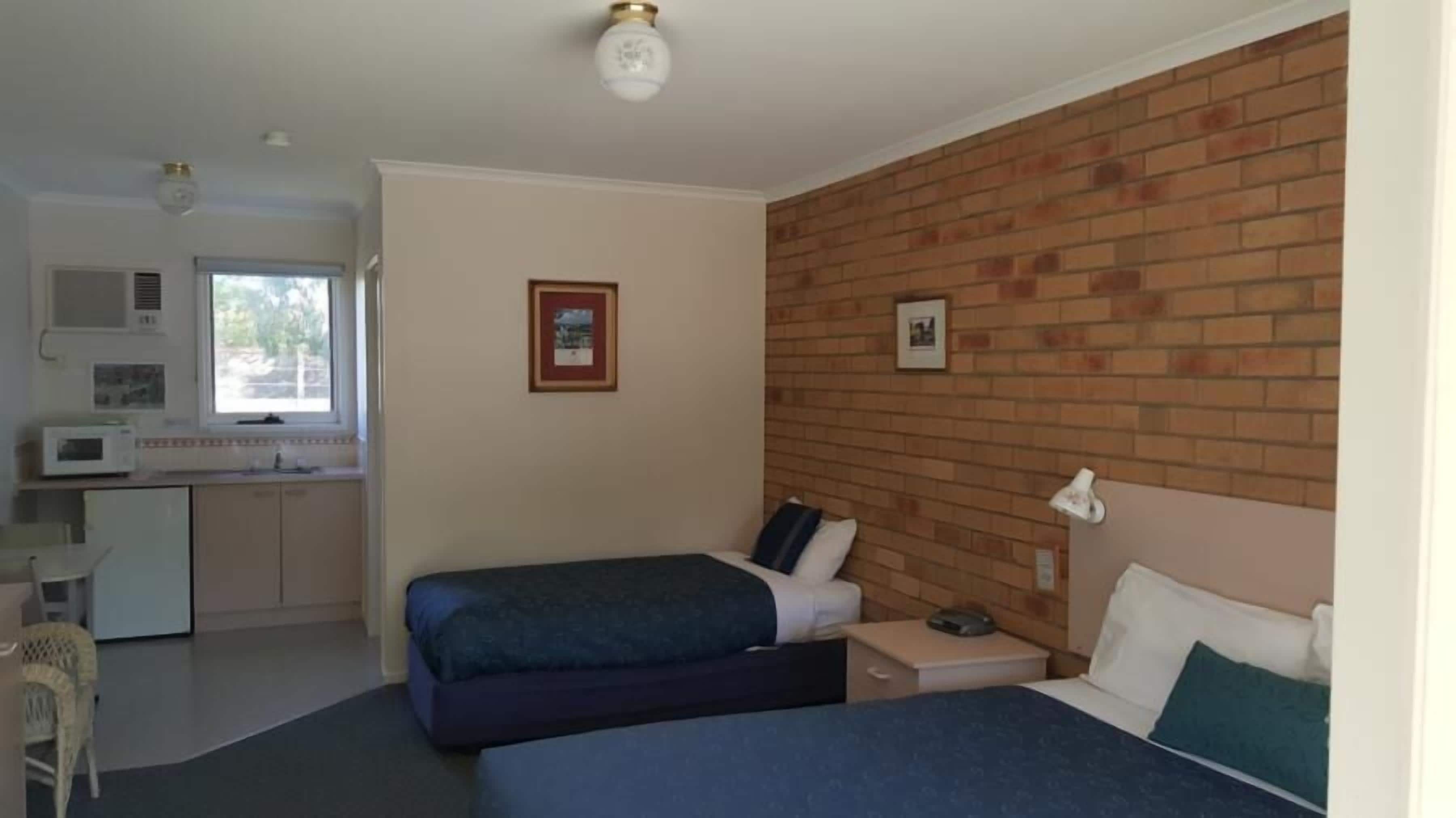 Ein Zimmer mit zwei Betten, einer Küchenzeile und einer Backsteinwand.