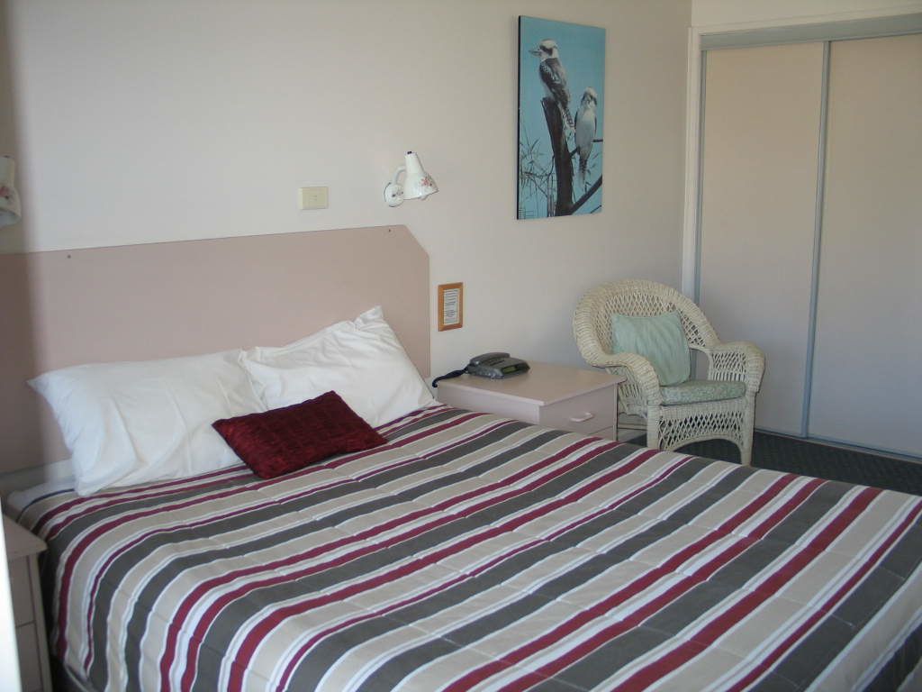 Un dormitorio con cama, una silla, un cuadro y un armario.