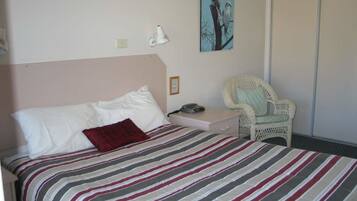 Un dormitorio con cama, una silla, un cuadro y un armario.