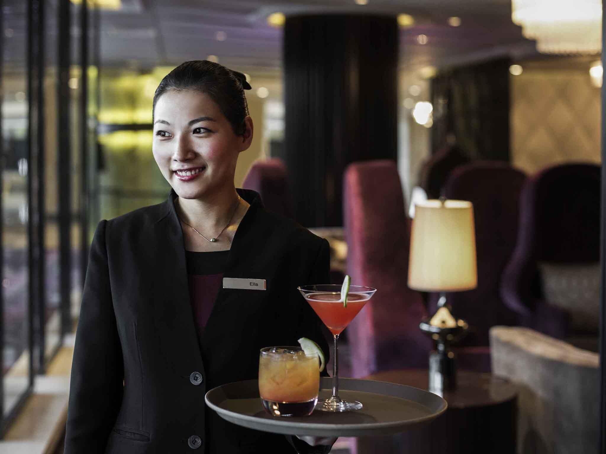 Un miembro del personal de hotel sostiene una bandeja con un martini y un cóctel.