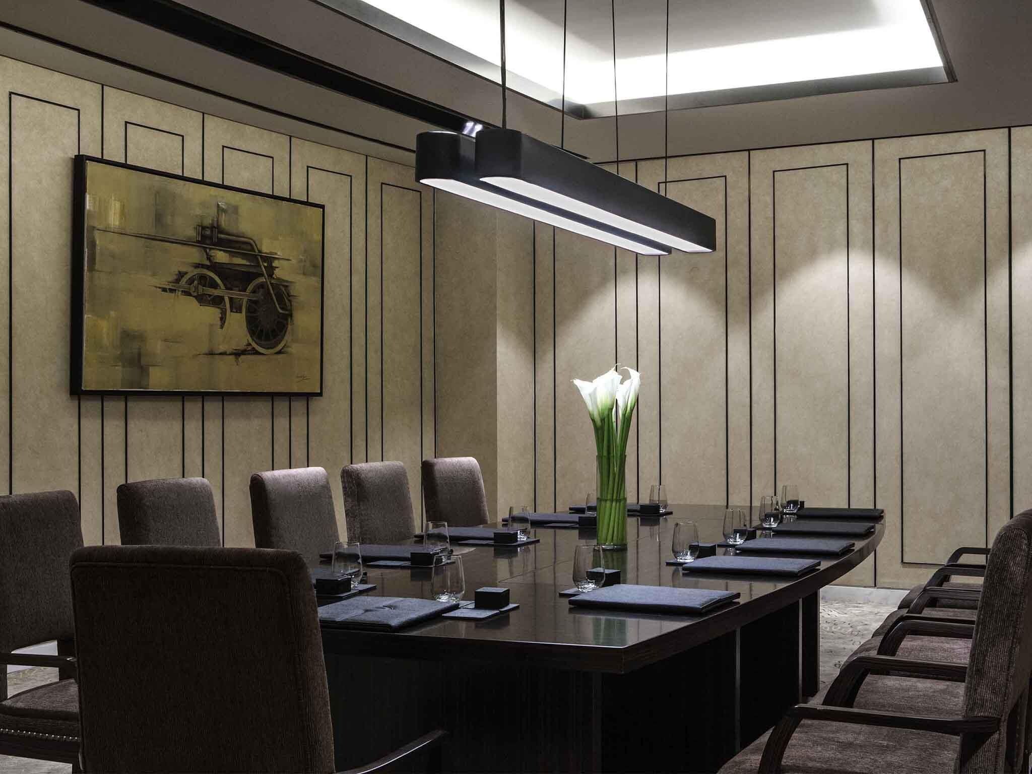 A conference room with a long table, chairs, a vase with white flowers, and a painting on the wall.