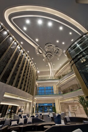 Eine moderne Hotelhalle mit gewölbter Decke, Sitzbereichen und einem großen Kronleuchter.