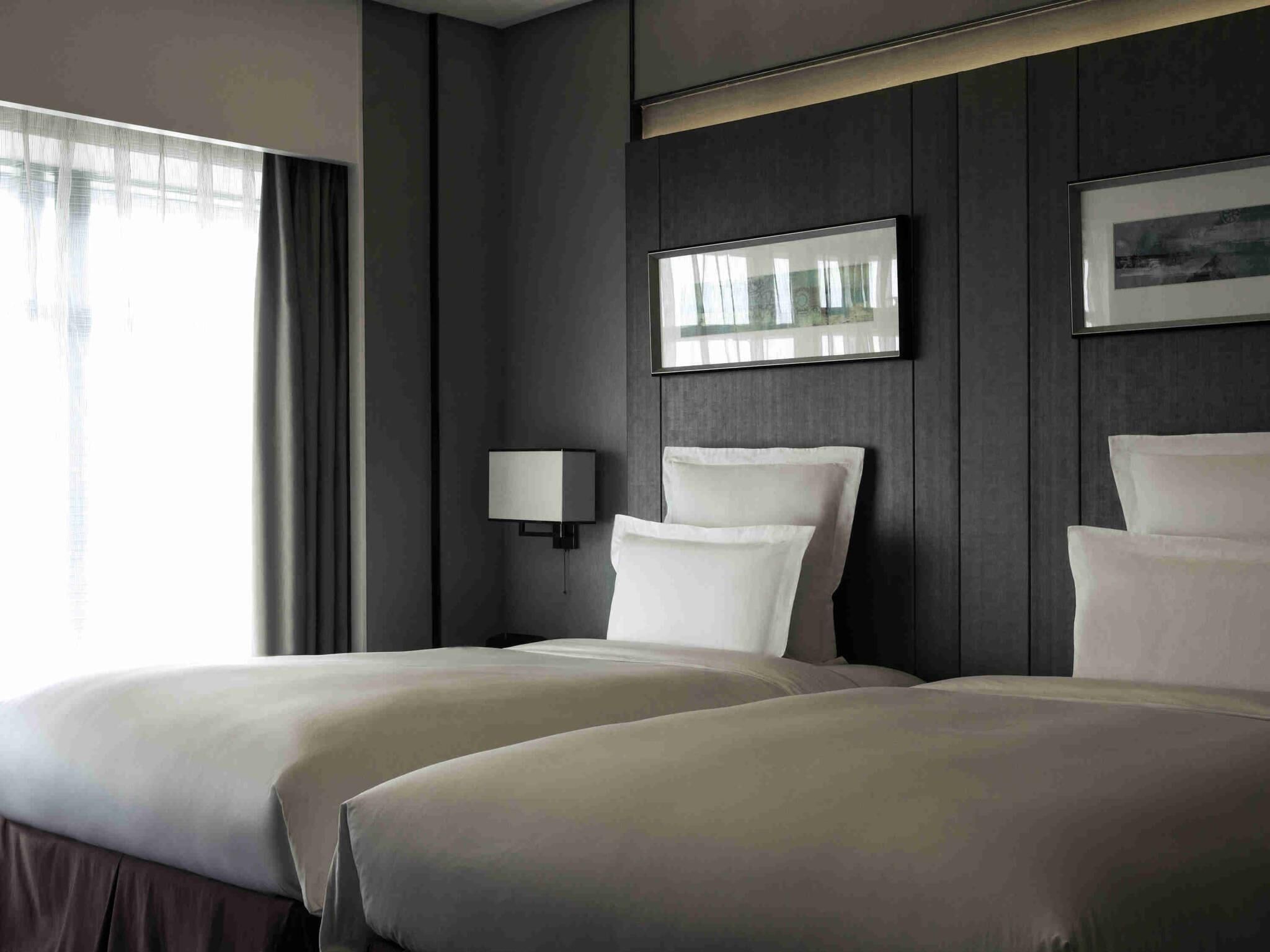 A hotel room with two beds, a bedside lamp, a framed picture on the wall, and a window with curtains.