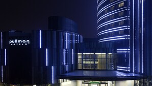 A modern hotel with a curved facade and illuminated lines, a prominent entrance, and a landscaped area with a water feature. - Pullman Shanghai Xuhui (Shanghai)