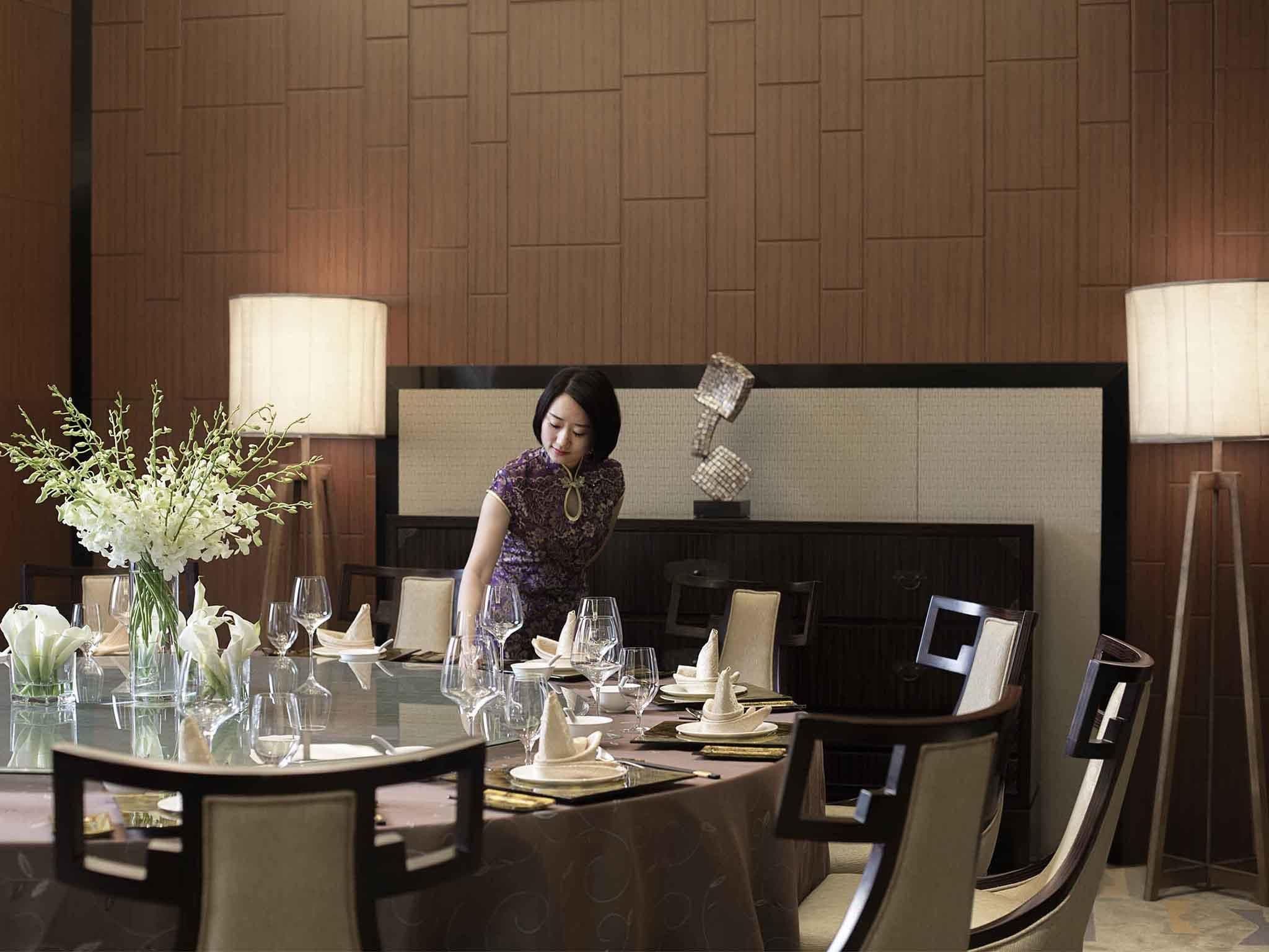 A dining area with a round table set for a meal, a vase with white flowers, and a decorative wall piece.