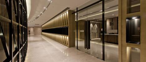 Un couloir d’hôtel moderne avec un sol réfléchissant, des portes en verre et un espace de réception.