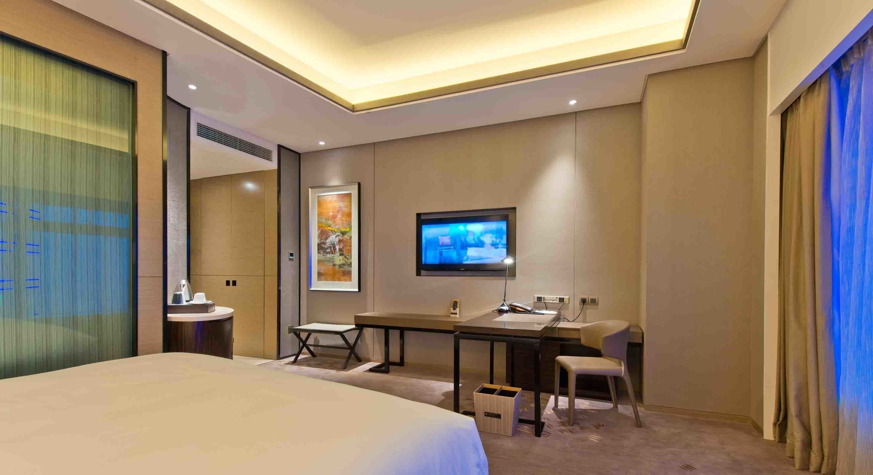 A hotel room with a bed, a desk, a chair, a television, and a small table.