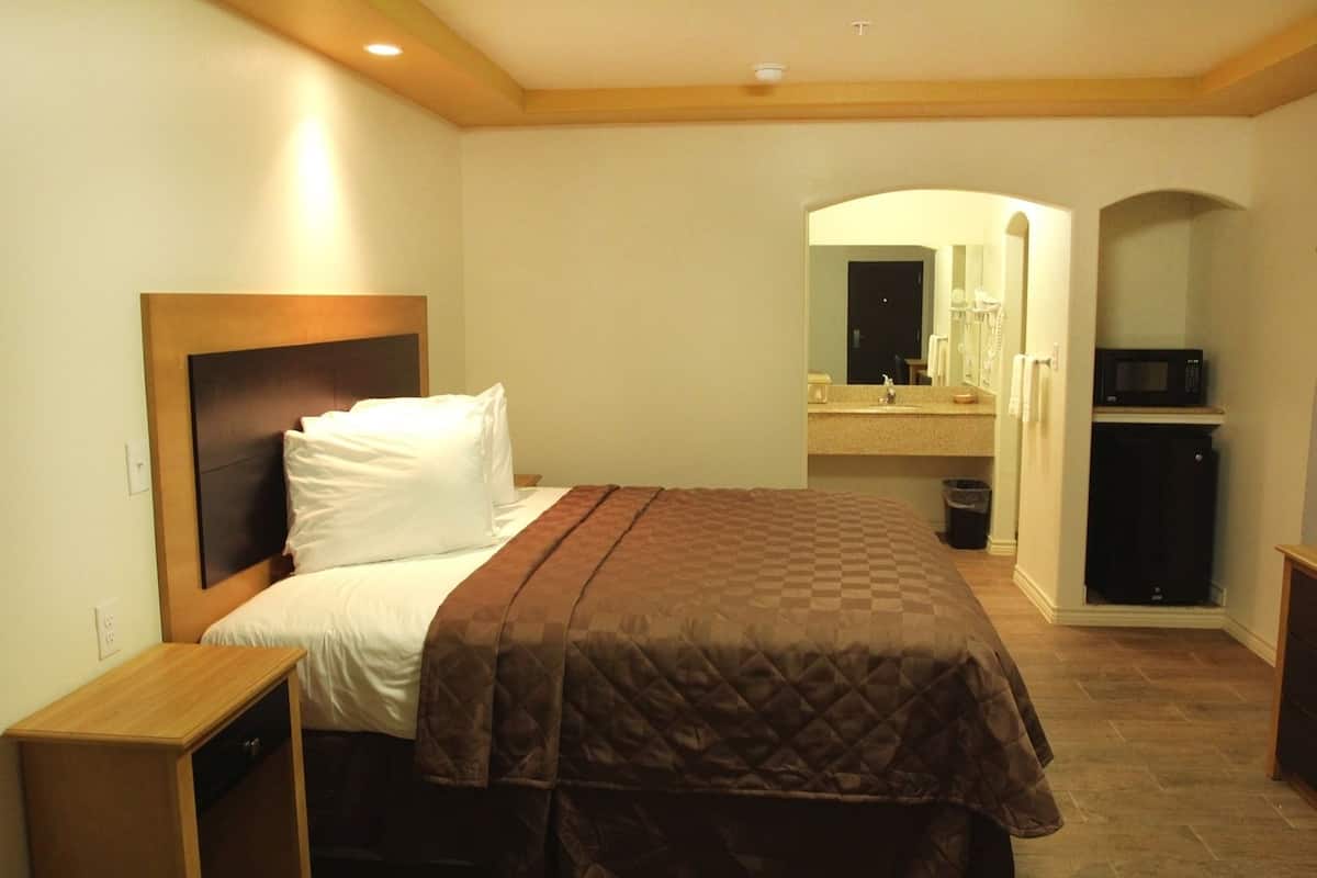 Un dormitorio con cama, mesita de noche, cómoda, microondas y un baño visible a través de un arco.