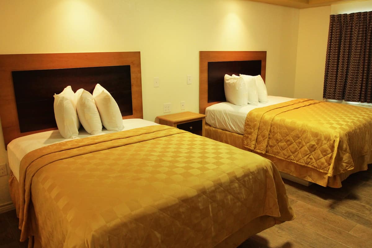 Habitación de hotel con dos camas, cada una con cabecera y mesita de noche.