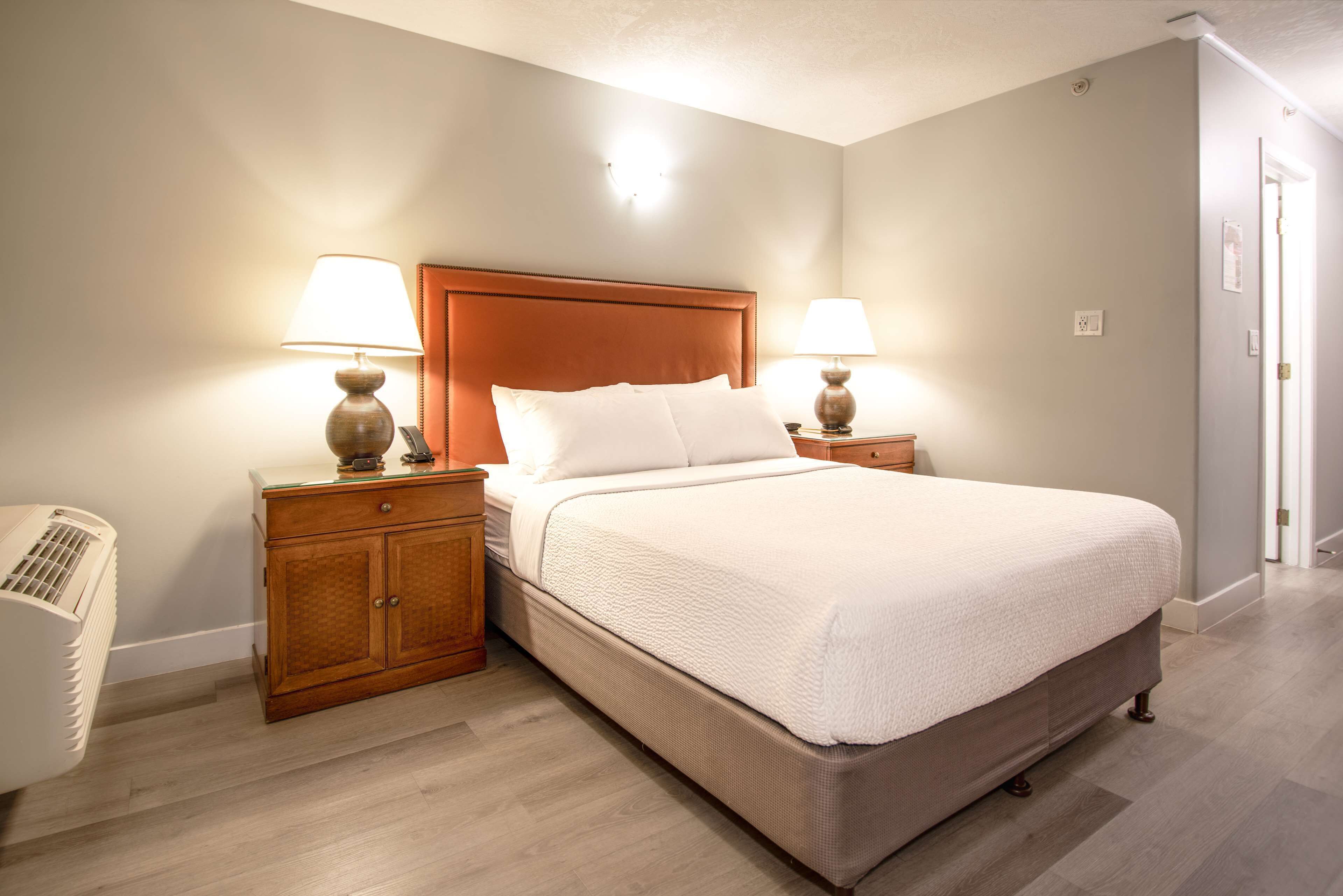A neatly arranged bedroom with a large bed, two bedside tables with lamps, a wooden nightstand, and a wall-mounted heater.