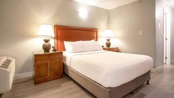 A neatly arranged bedroom with a large bed, two bedside tables with lamps, a wooden nightstand, and a wall-mounted heater.