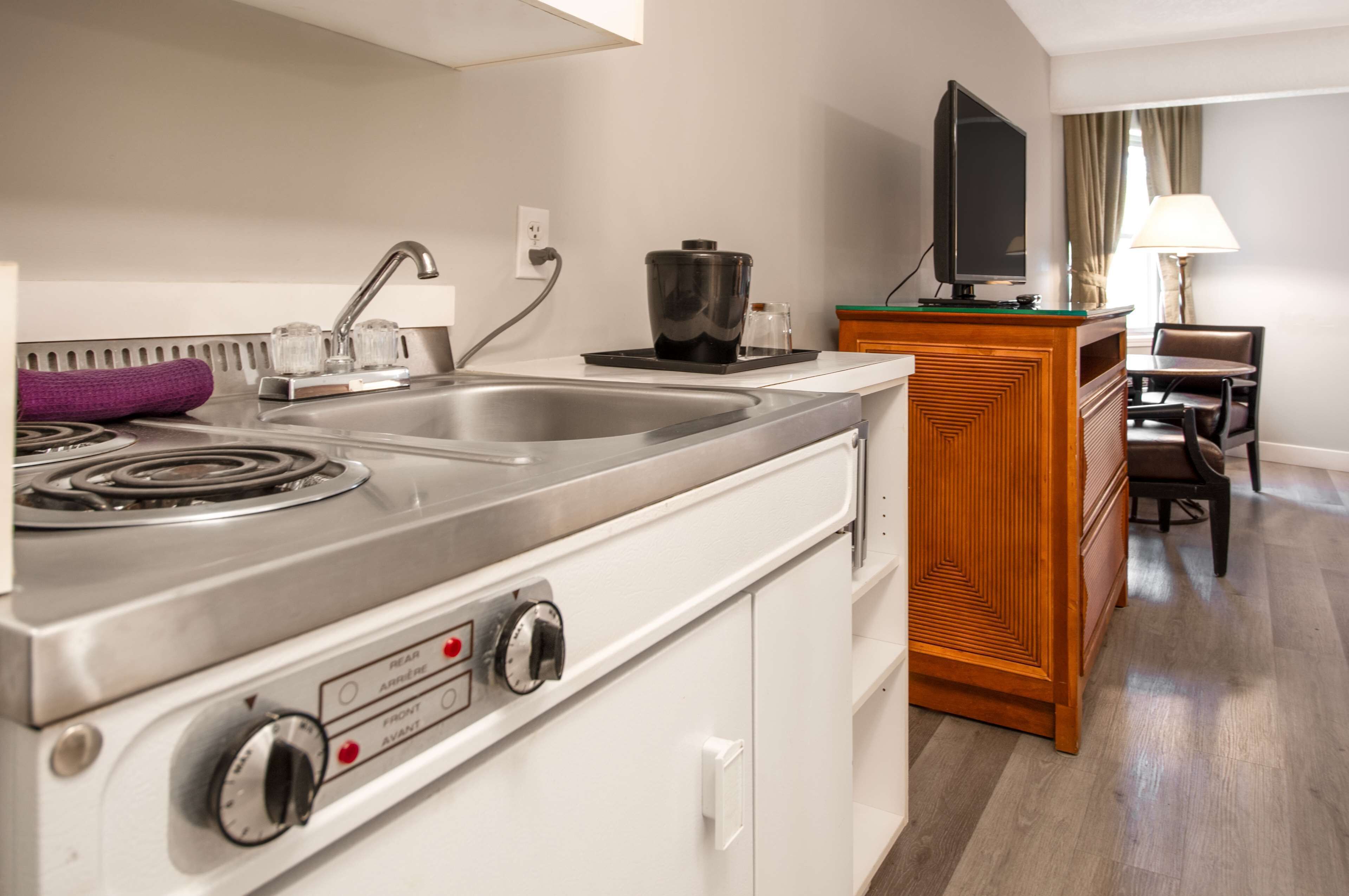 A kitchen with a stove, sink, and a television on a wooden cabinet.