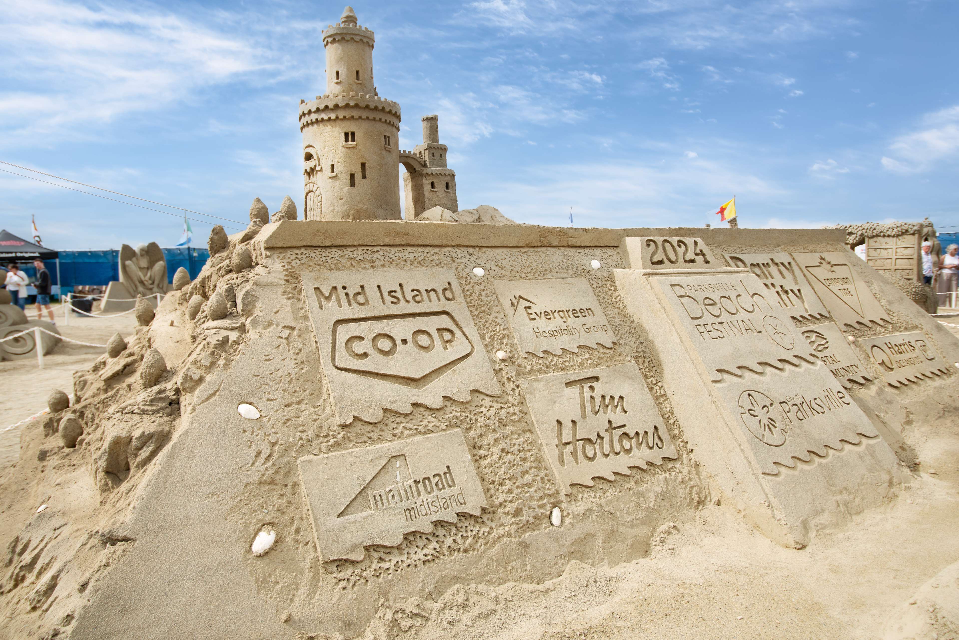 A sandcastle with labels indicating 'Mid Island CO-OP,' 'Tim Hortons,' 'Evergreen Hospitality Group,' and '2024 Beach City Festival.'