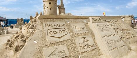 A sandcastle with labels indicating 'Mid Island CO-OP,' 'Tim Hortons,' 'Evergreen Hospitality Group,' and '2024 Beach City Festival.'