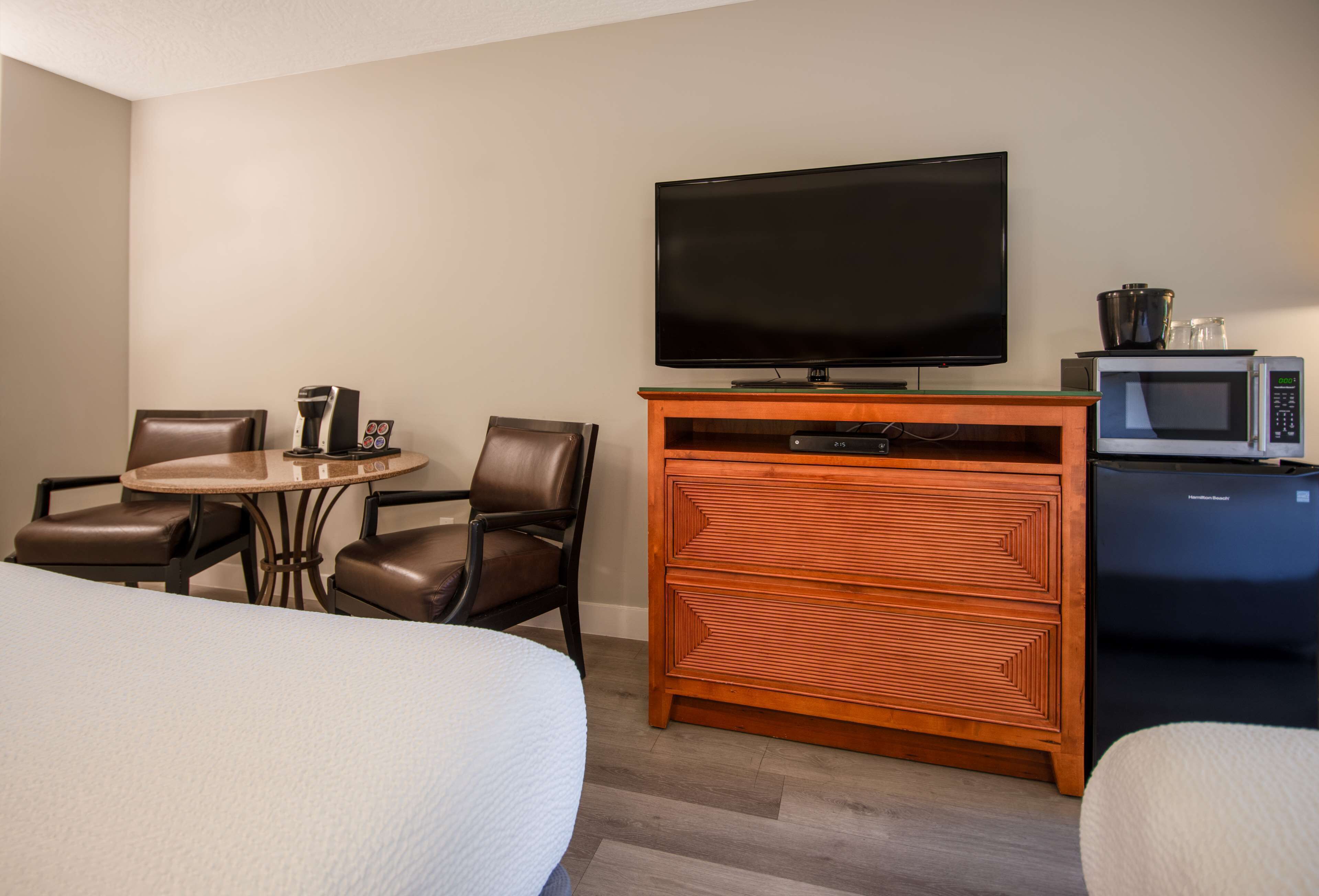 A hotel room with a bed, a round table with chairs, a TV, a microwave, and a wooden cabinet.