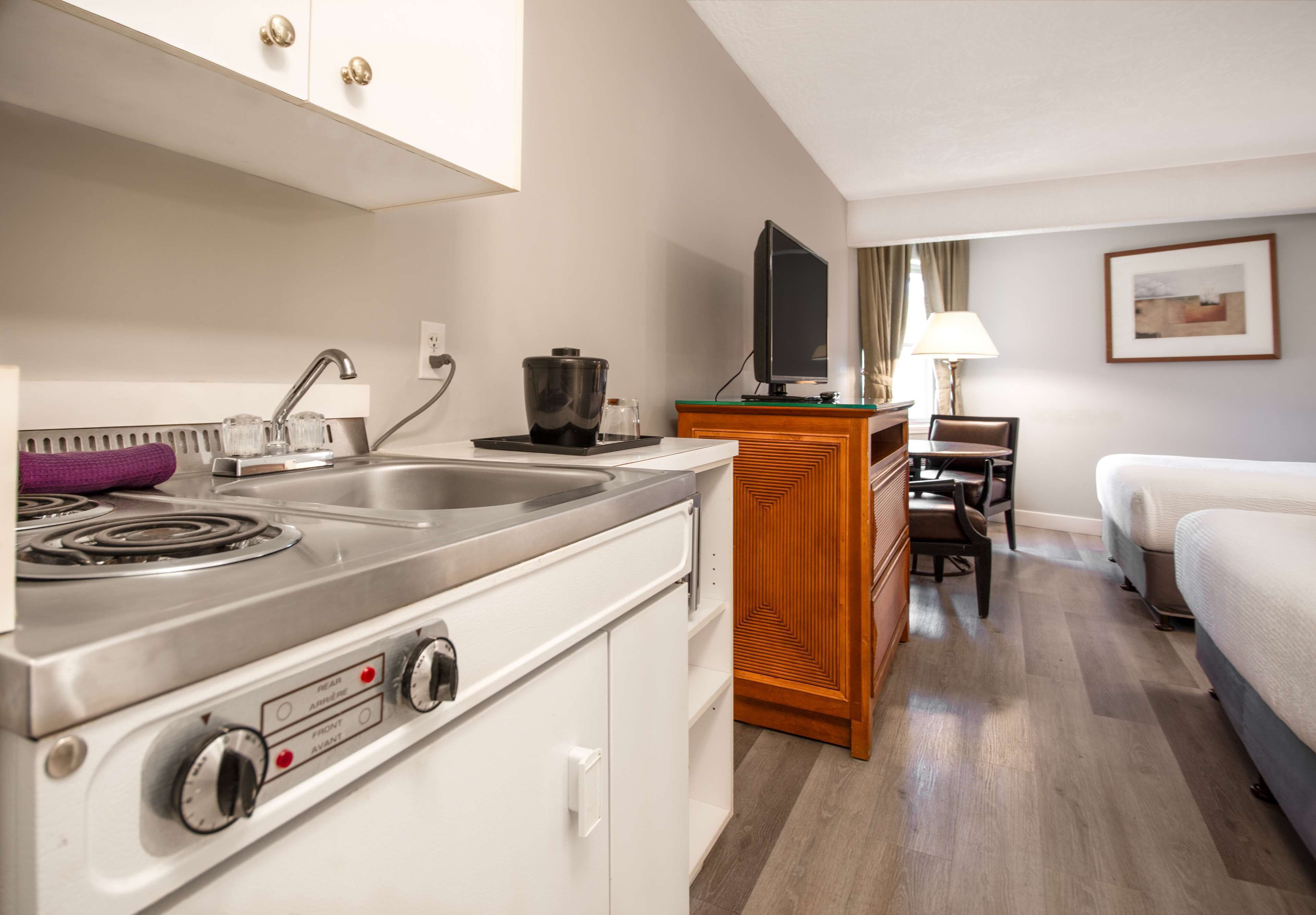 A compact hotel room with a kitchenette, a bed, a TV, and a small desk area.
