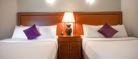 A hotel room with two beds, a nightstand with a lamp, and a wooden headboard.