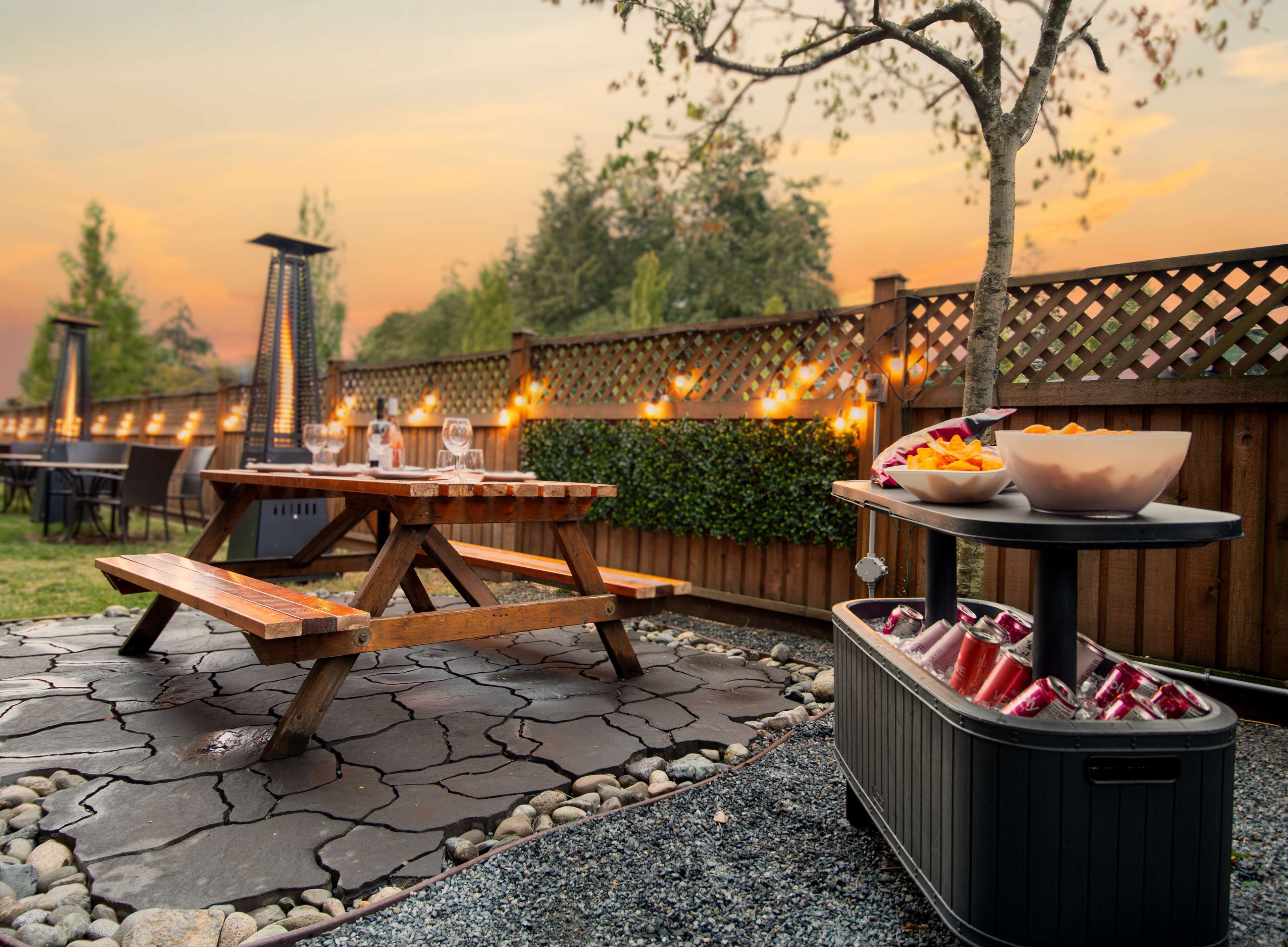 Une terrasse extérieure avec des tables et des bancs en bois, un barbecue et une poubelle.