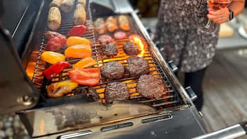 Une personne qui fait griller différents types de viande et de légumes sur un barbecue extérieur.