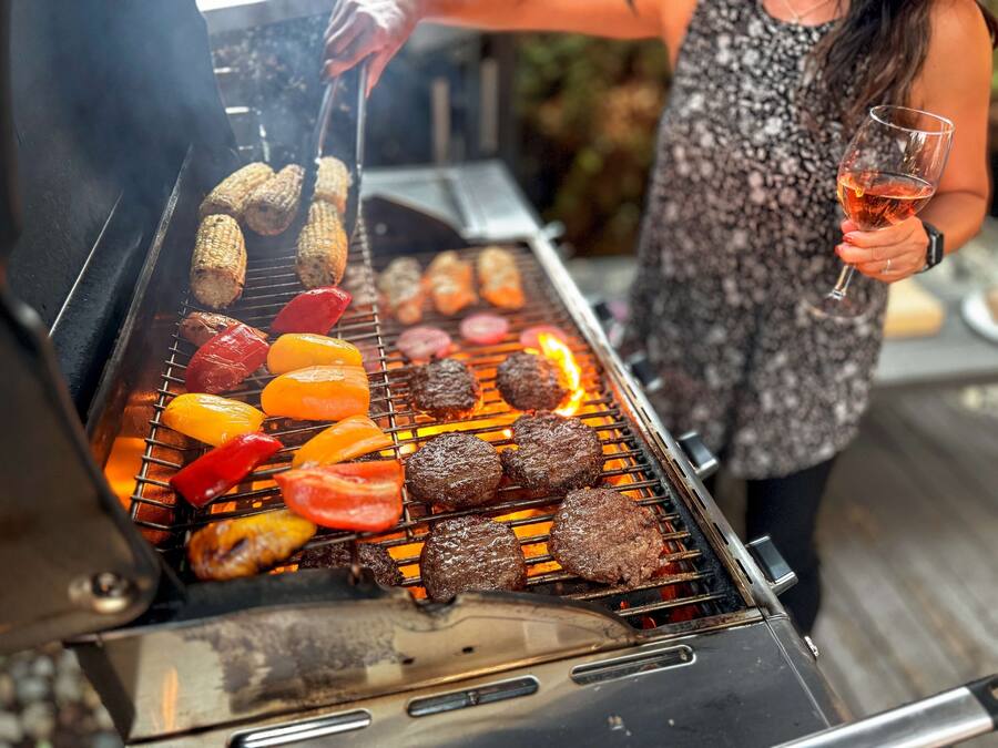 Eine Person grillt verschiedene Fleisch- und Gemüsesorten auf einem Grill im Freien.