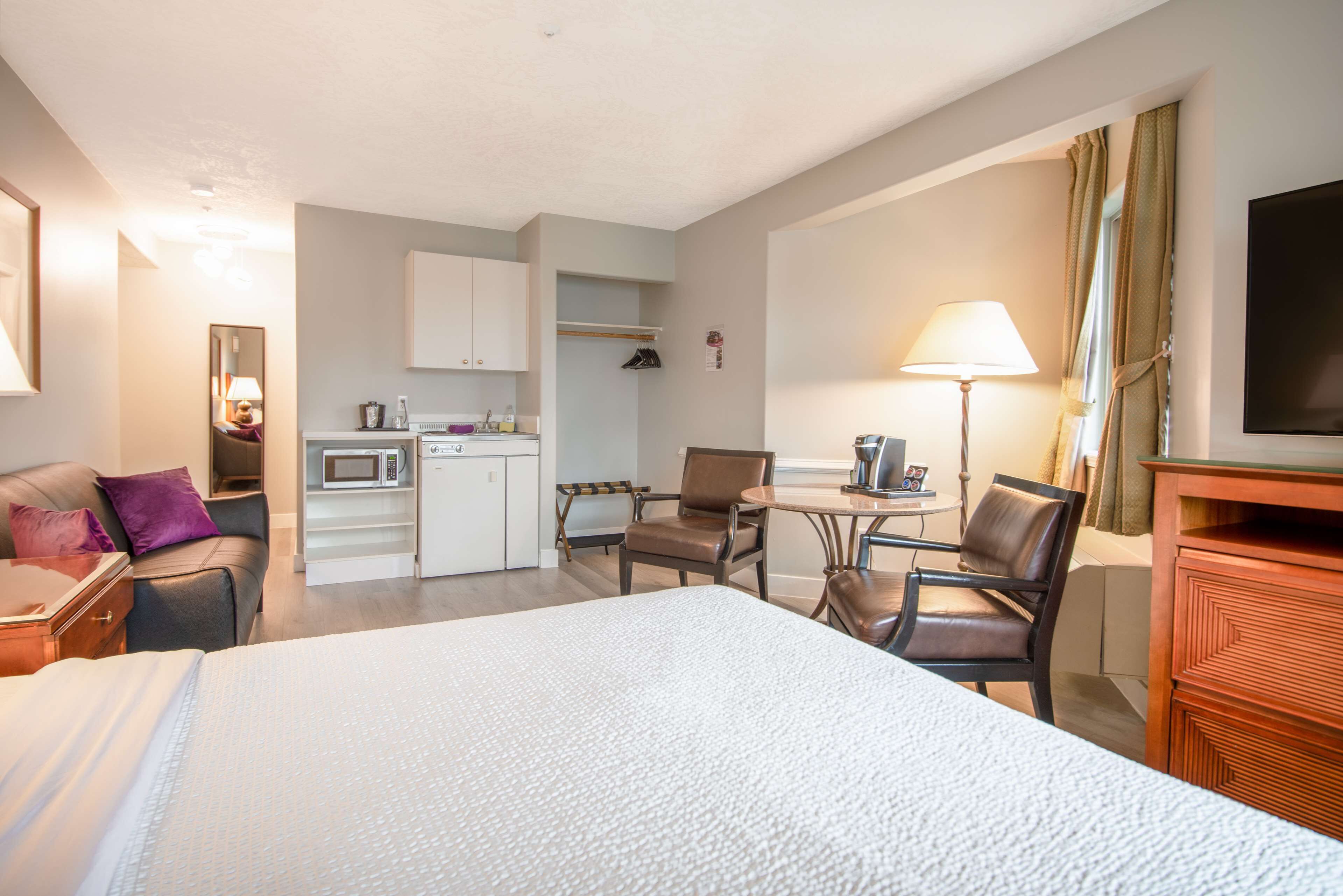 A hotel room with a bed, a desk, a chair, a small kitchenette, and a TV.