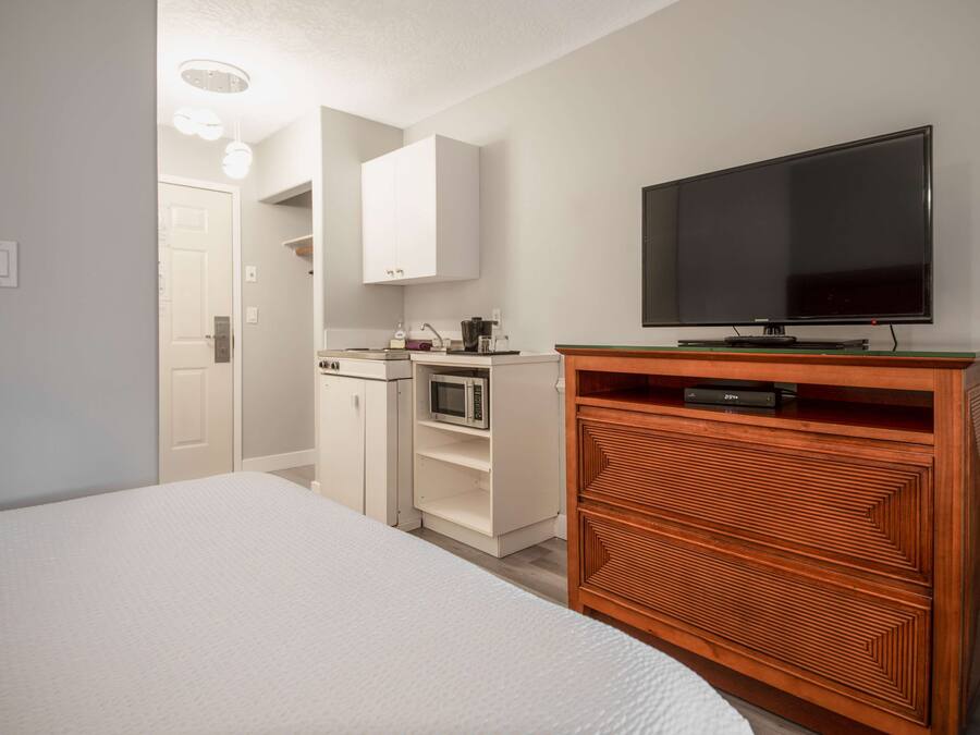 Ein Schlafzimmer mit einem Bett, einer Holzkommode, einem Fernseher, einer Mikrowelle und einer Tür zu einem Badezimmer.