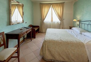 A hotel room with a bed, a desk, a chair, a mirror, and a window with curtains. - Hotel Villa Luigi (Martinsicuro)