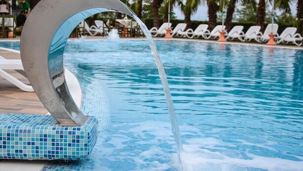 Ein Pool mit Wasserspiel, umgeben von Liegestühlen und Sonnenschirmen.
