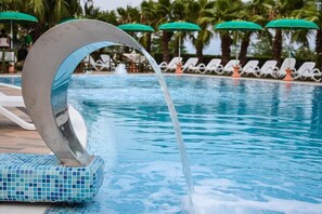A swimming pool with a water feature, surrounded by lounge chairs and umbrellas. - Hotel Villa Luigi (Martinsicuro)