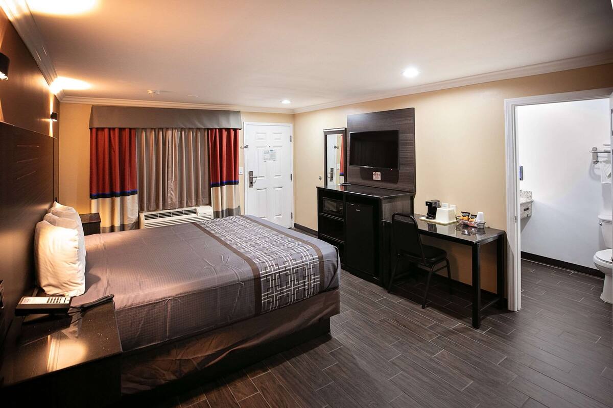 Una habitación de hotel con cama, escritorio, televisor, espejo y baño.