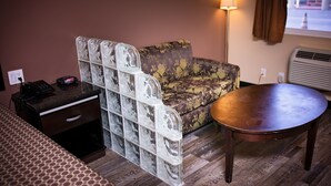 A compact hotel room with a sofa, a small table, a bedside table with a phone, and a lamp. - Rodeway Inn & Suites Bellflower (Bellflower)