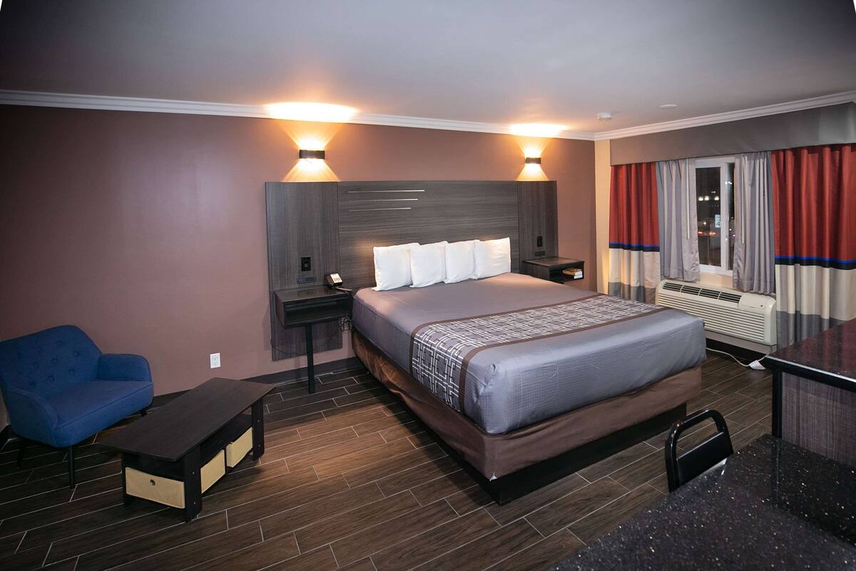 Habitación de hotel con una cama grande, mesitas de noche, un escritorio, una silla, un sofá y una ventana con cortinas.
