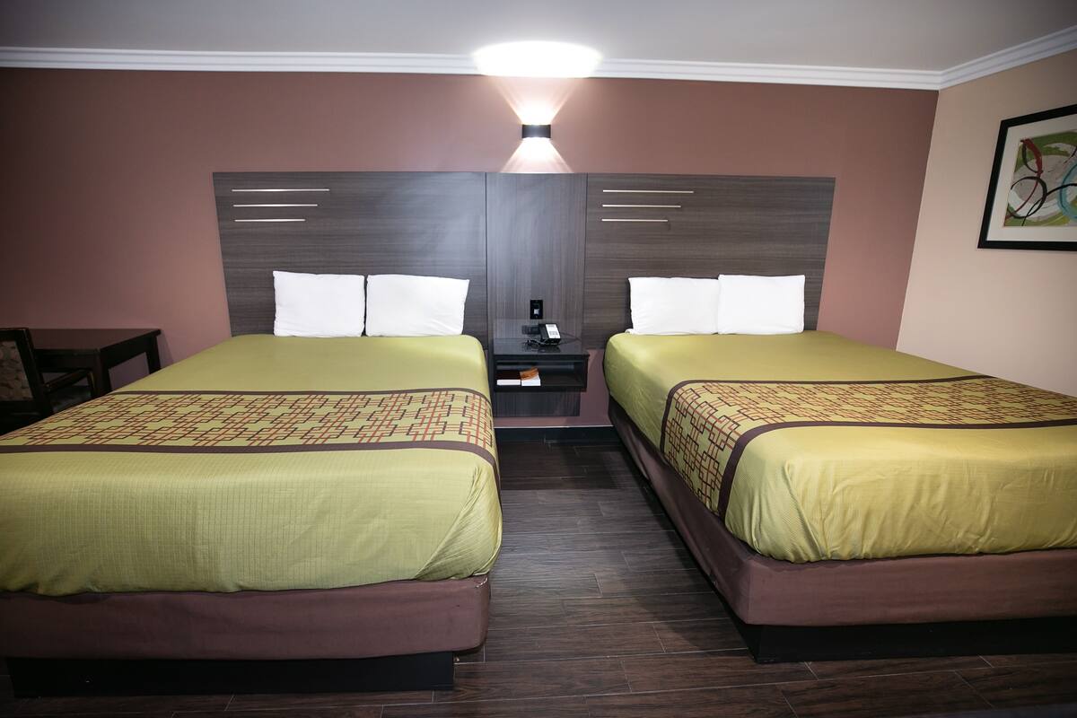 Una habitación de hotel con dos camas, una mesita de noche y una lámpara de pared.