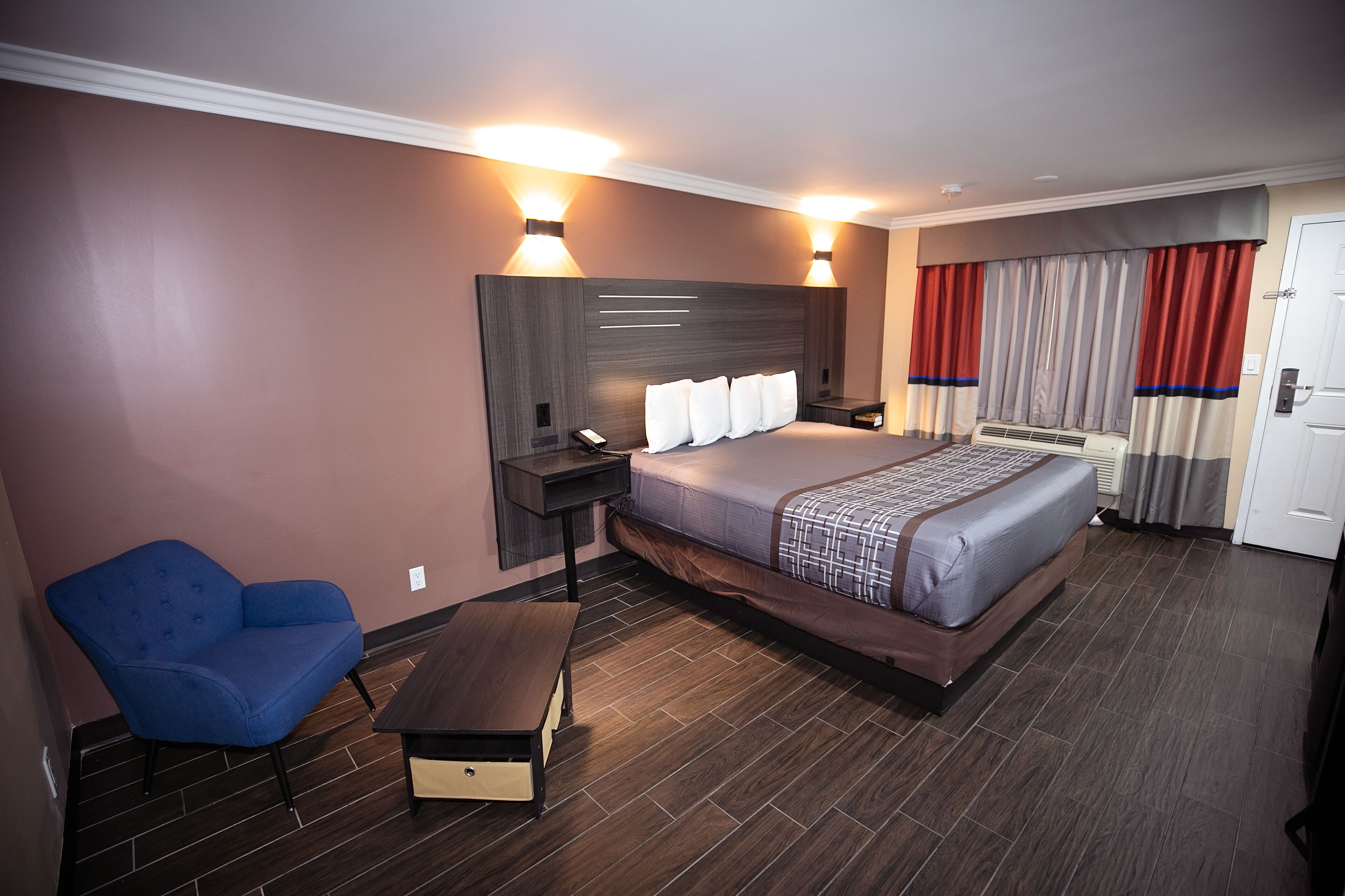 A hotel room with a bed, bedside tables, a chair, a bench, and a wall-mounted TV.