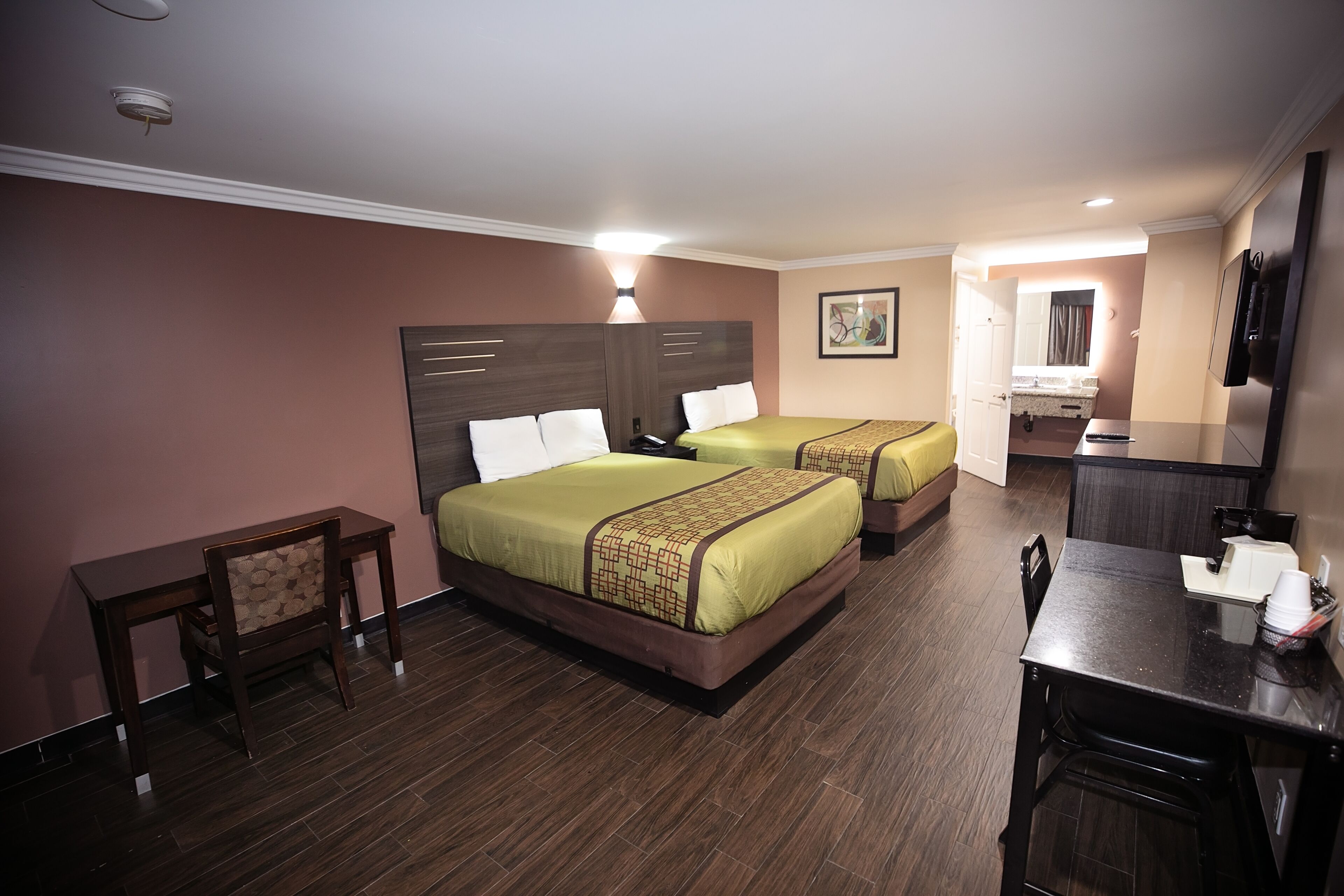 A hotel room with two beds, a desk, a chair, a television, and a bathroom visible through an open door.