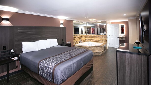 A modern hotel room with a large bed, a separate bathroom with a bathtub, and a flat-screen TV. - Rodeway Inn & Suites Bellflower (Bellflower)