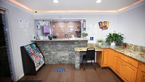 A reception area with a stone wall, a counter, a computer, and a plant. - Rodeway Inn & Suites Bellflower (Bellflower)