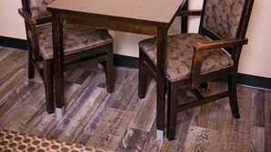 A dining area with a table and four chairs, a framed abstract painting on the wall, and a patterned rug on the floor. - Rodeway Inn & Suites Bellflower (Bellflower)