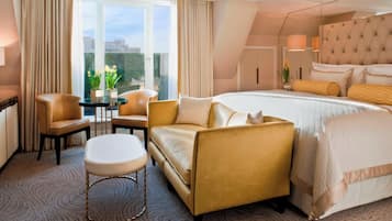 Habitación de hotel con una cama grande, dos sillones, una mesita y vistas a la ciudad a través de amplios ventanales.