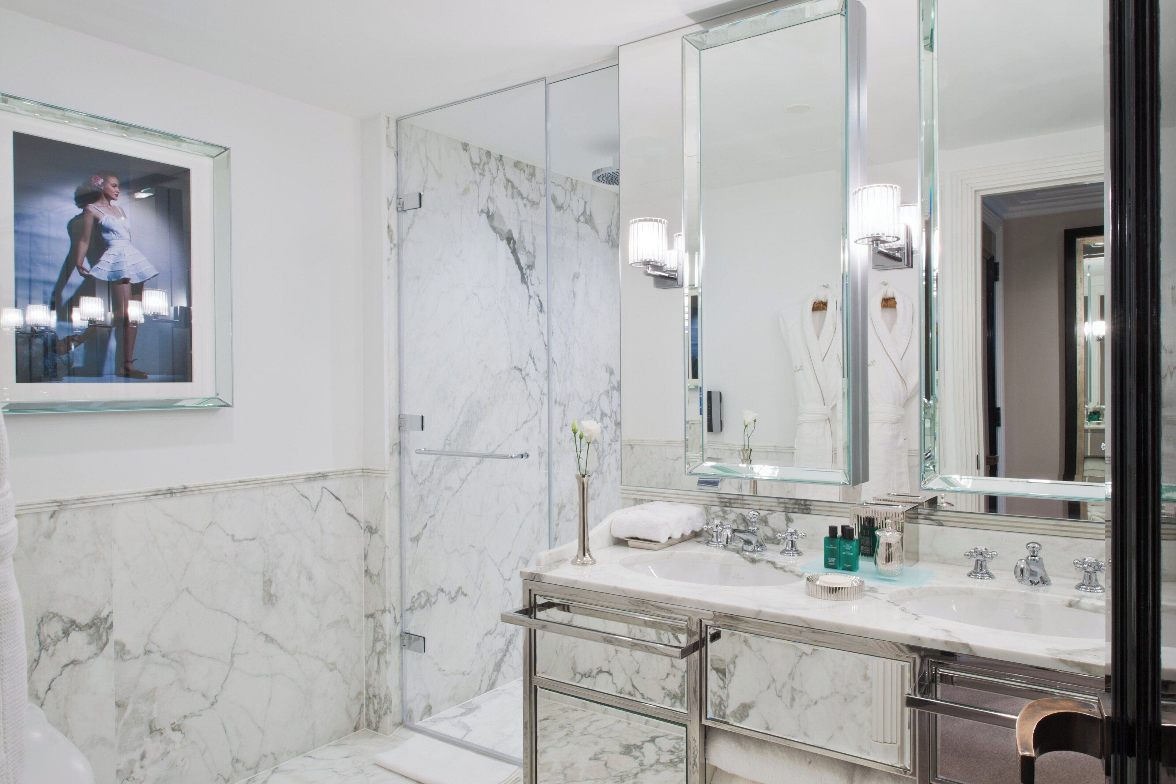 A modern bathroom with marble walls, a large mirror, and a glass shower enclosure.