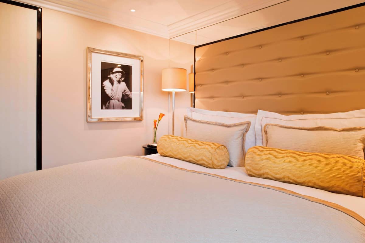 A neatly made bed with a tufted headboard, a framed picture on the wall, and a bedside lamp.