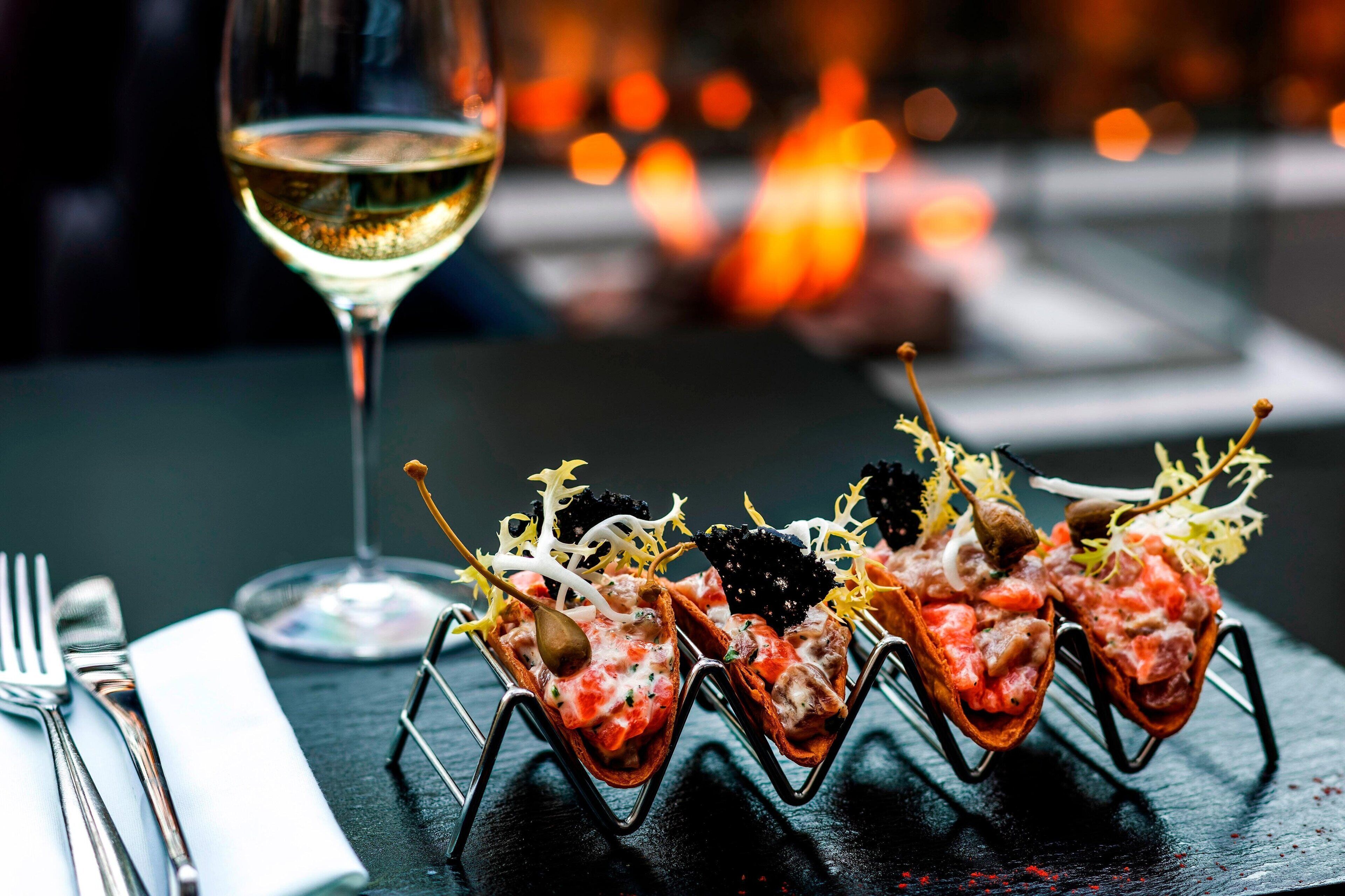 Una mesa con una copa de vino blanco, una servilleta y un plato de aperitivos.