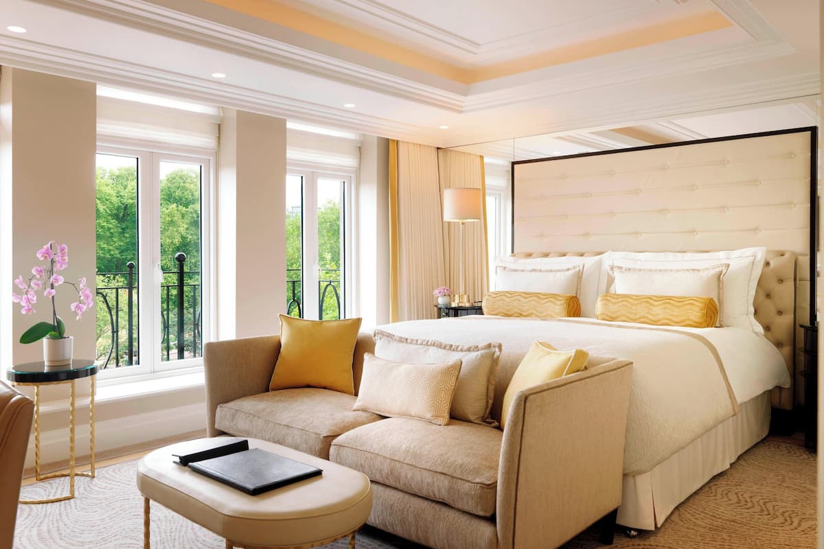 A hotel room with a large bed, a sofa, a small table, and a view of greenery outside.