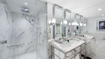 Une salle de bain moderne avec des murs en marbre, une cabine de douche en verre et un grand miroir au-dessus du lavabo.