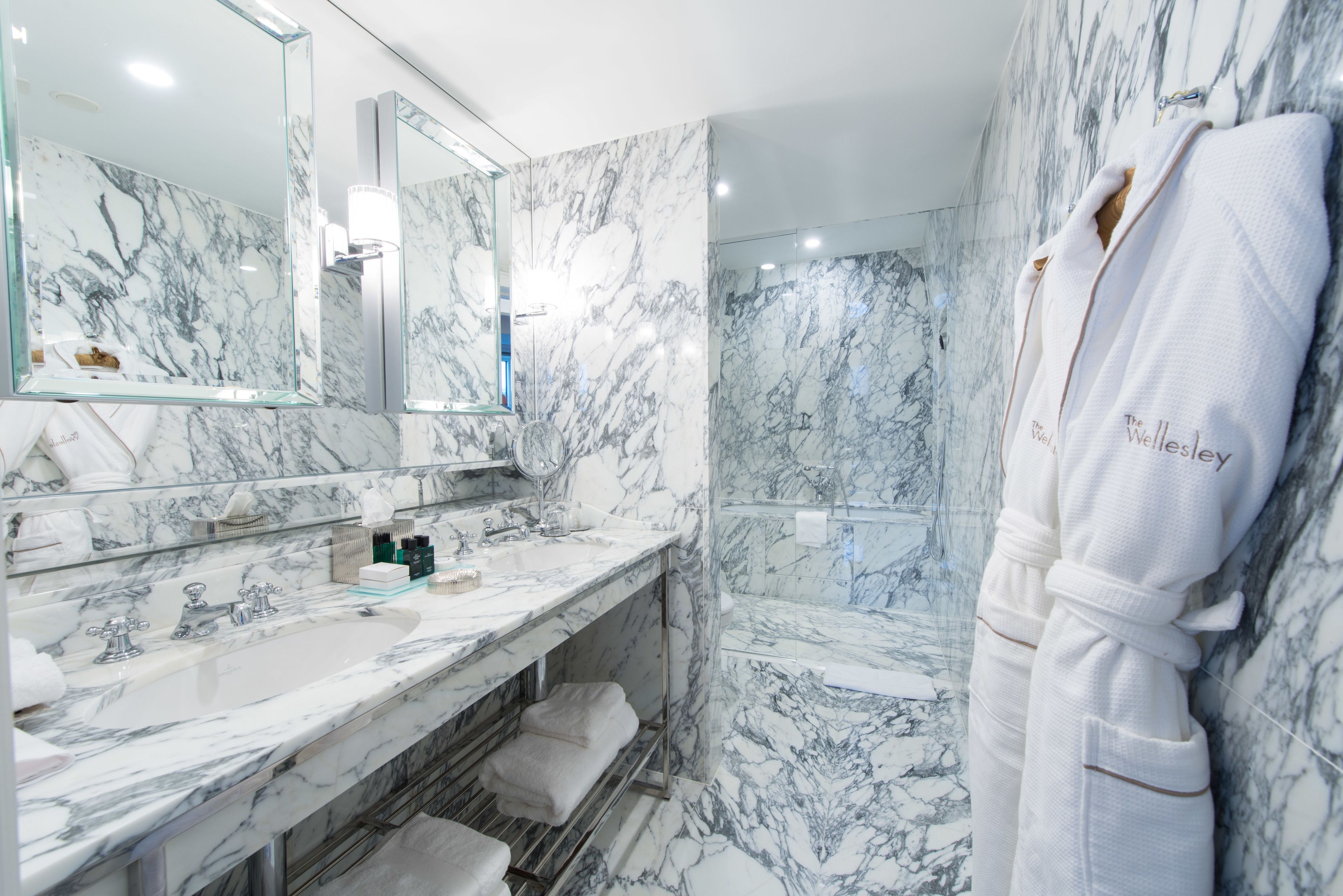 A marble bathroom with a large mirror, a sink, and a shower.