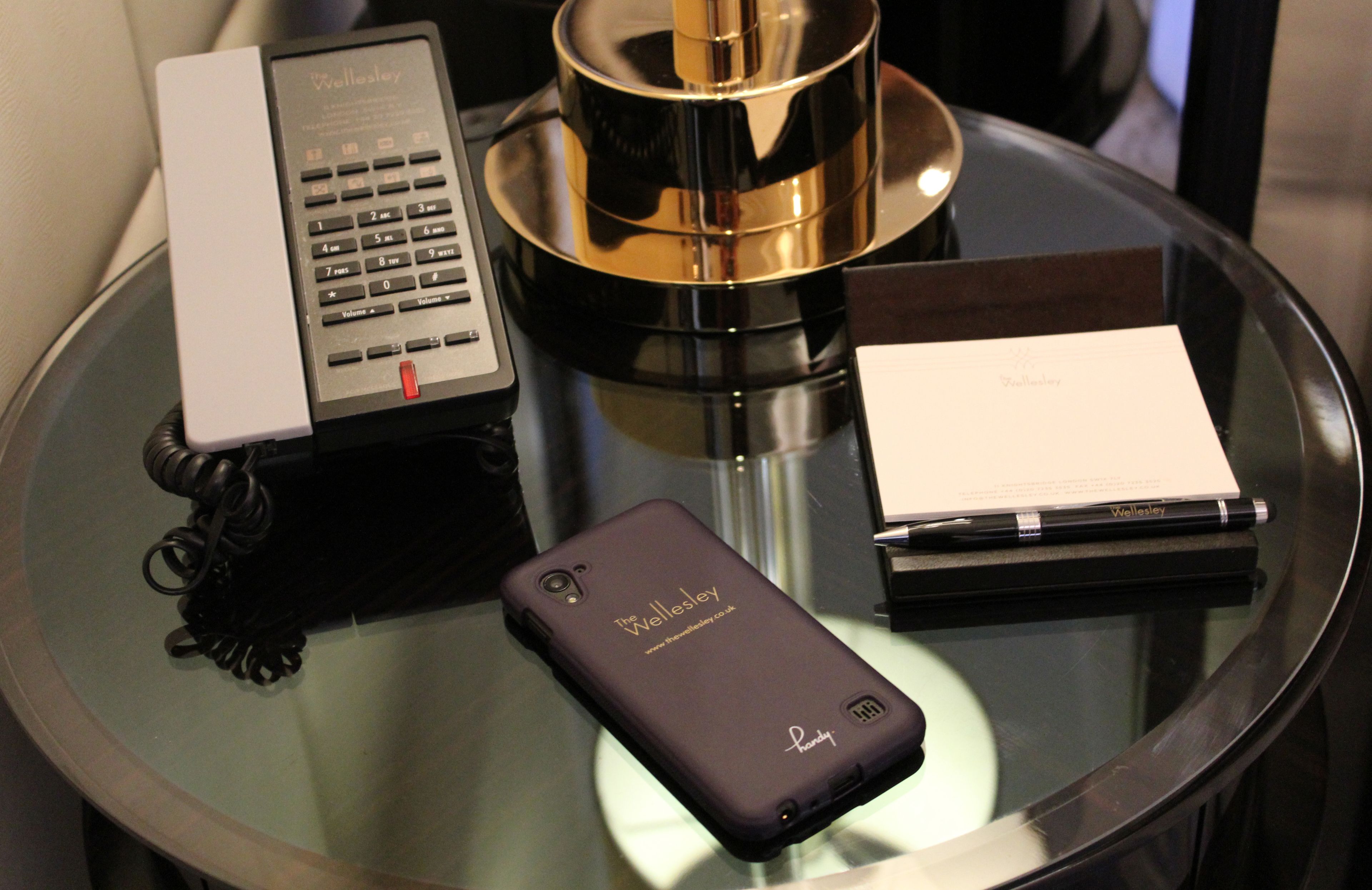 Une table en verre avec un téléphone noir, un stylo, un carnet et un téléphone.
