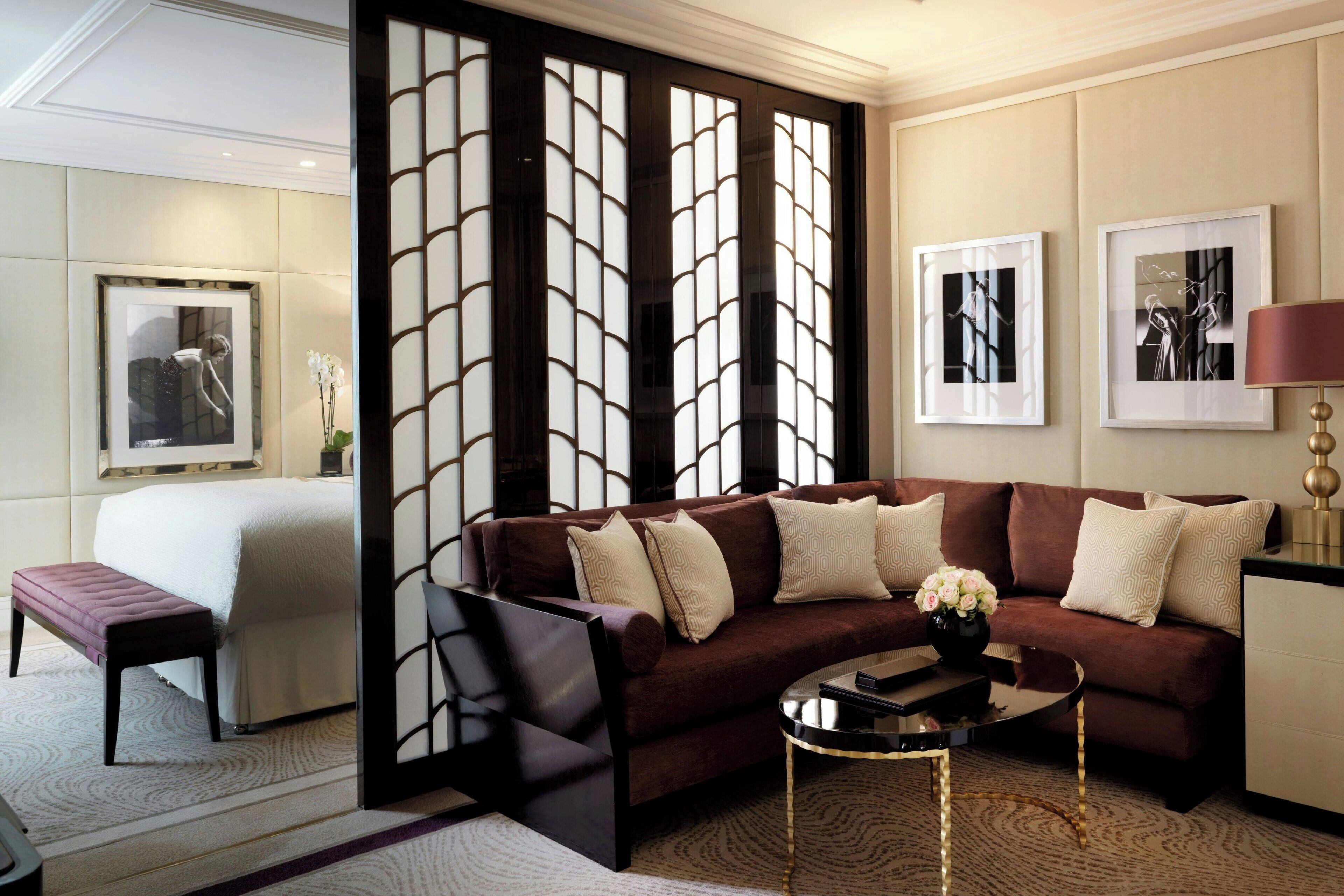 Une chambre d’hôtel moderne avec un grand lit, un canapé marron, une table basse et des œuvres d’art accrochées aux murs.