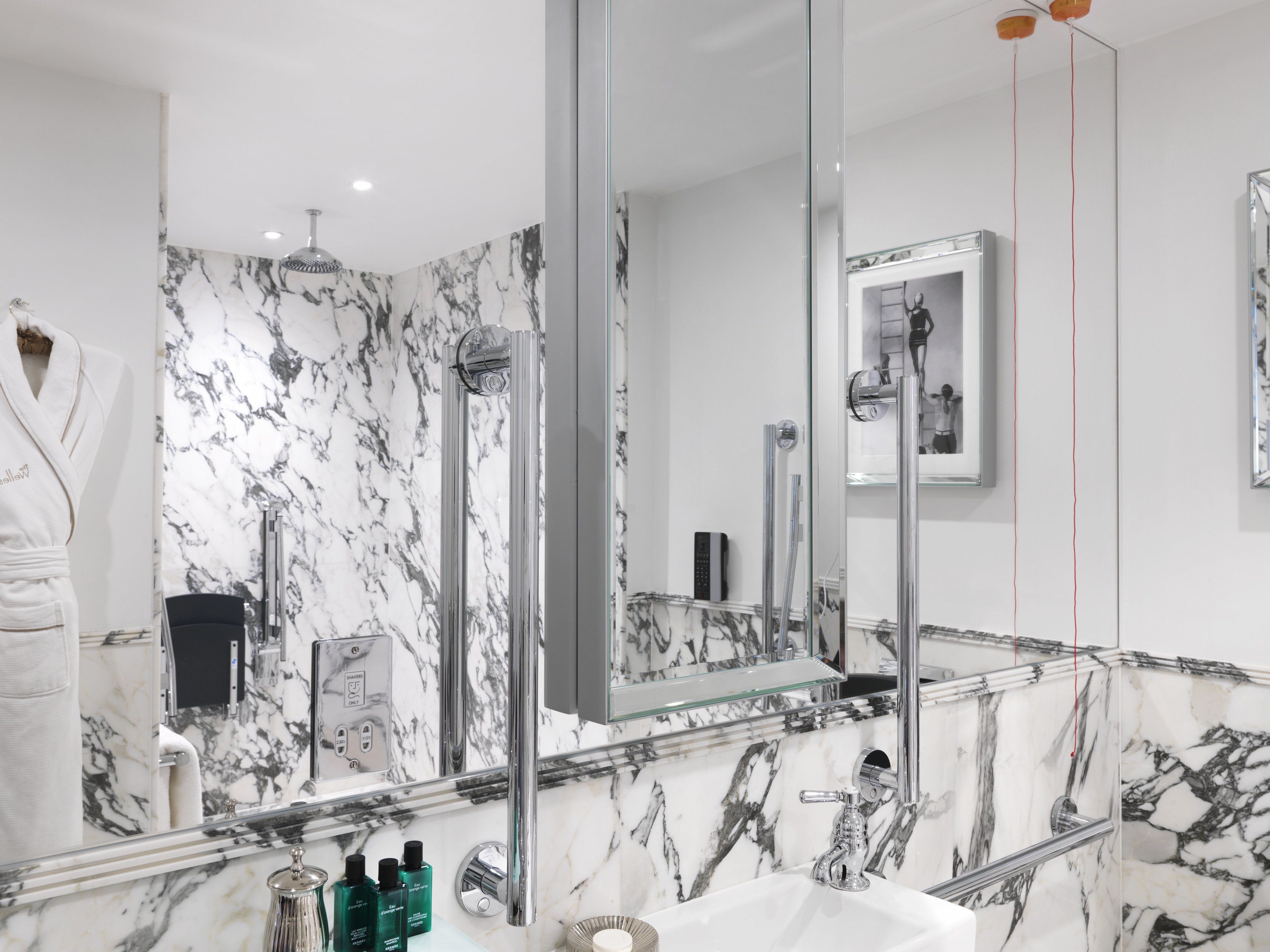 Een moderne badkamer met een grote spiegel, marmeren wanden en een douchecabine van glas.