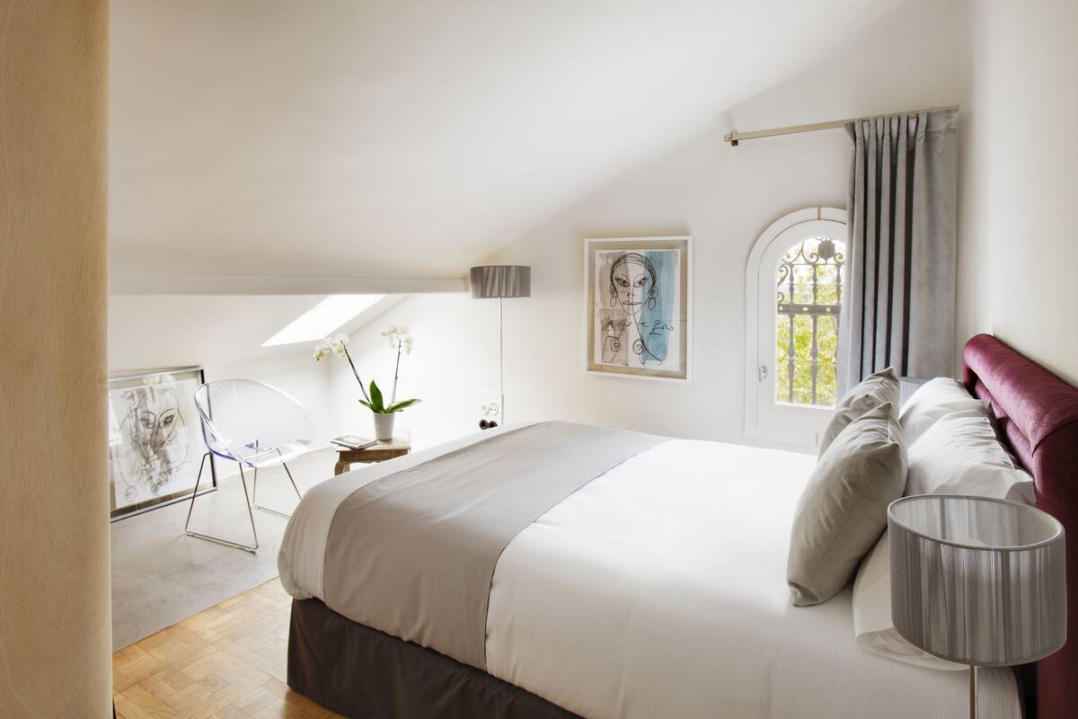 A bedroom with a large bed, a bedside lamp, a potted plant, and a window with curtains.