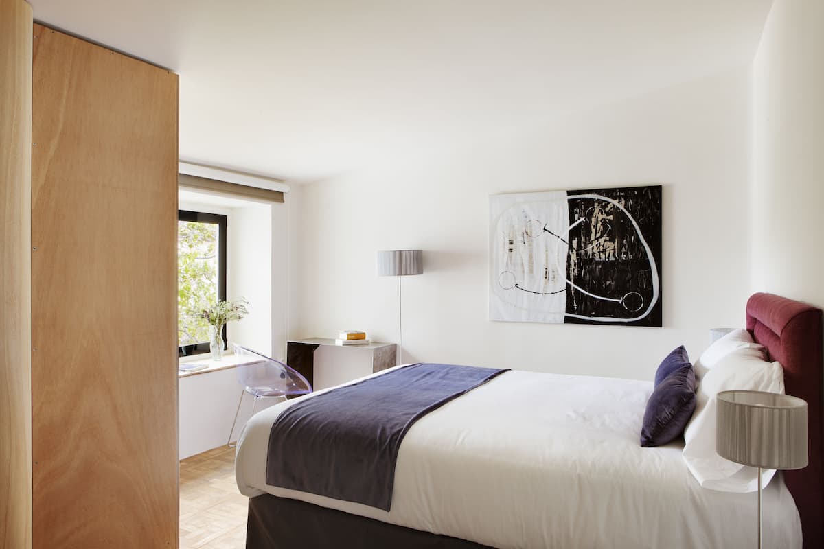 A modern bedroom with a large bed, a bedside table, a lamp, and a window with a view.